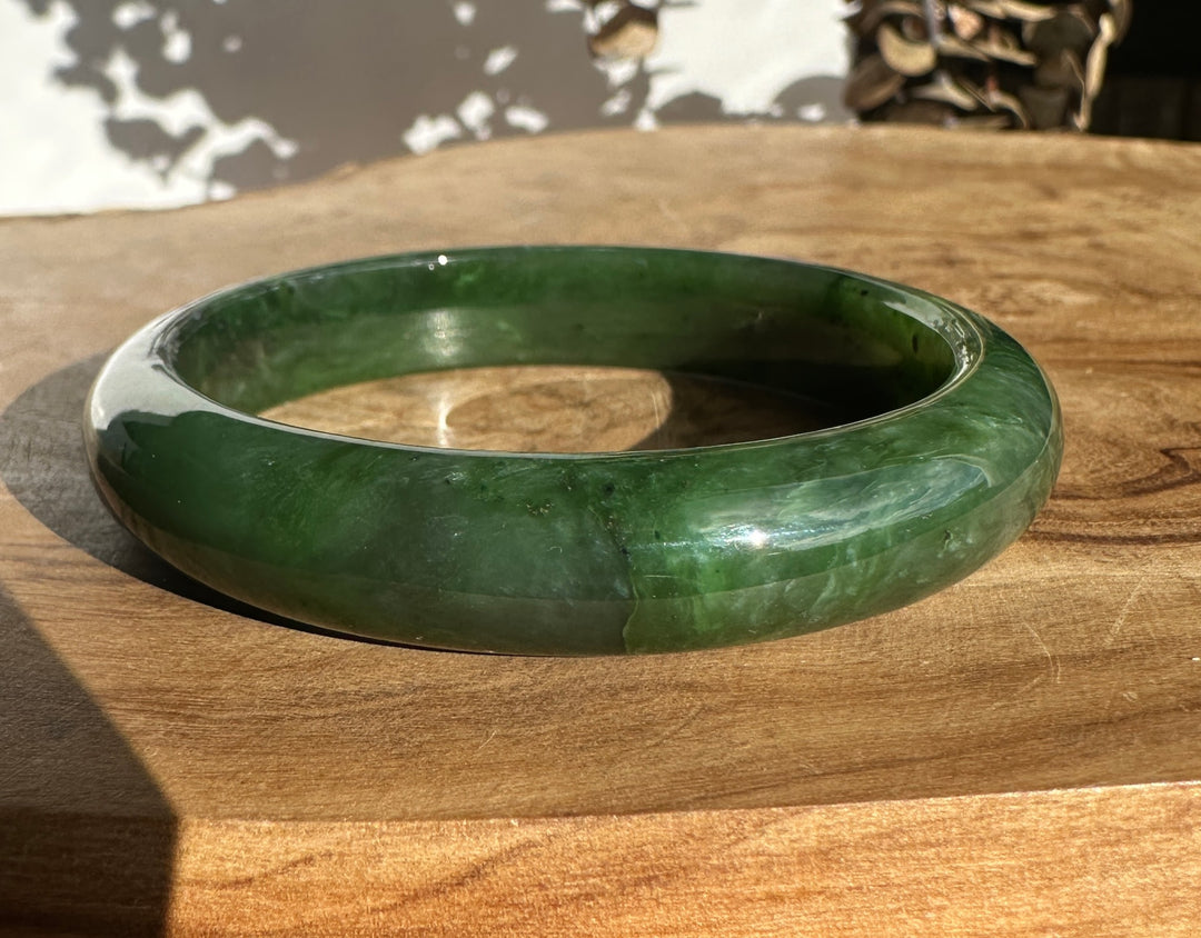 Green jade bangle resting on a wooden surface.