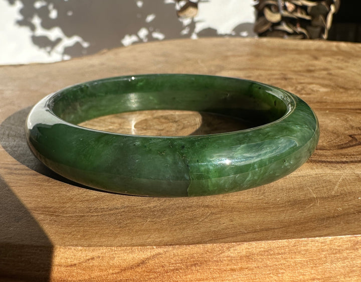 Green jade bangle resting on a wooden surface.