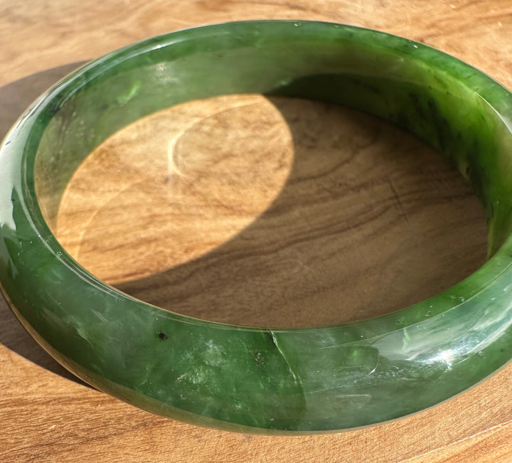 Close up of the green jade bangle edge on wood with a coin for scale.