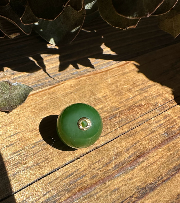 Polished green jade bead with a gold ring around the drilled hole resting on wood