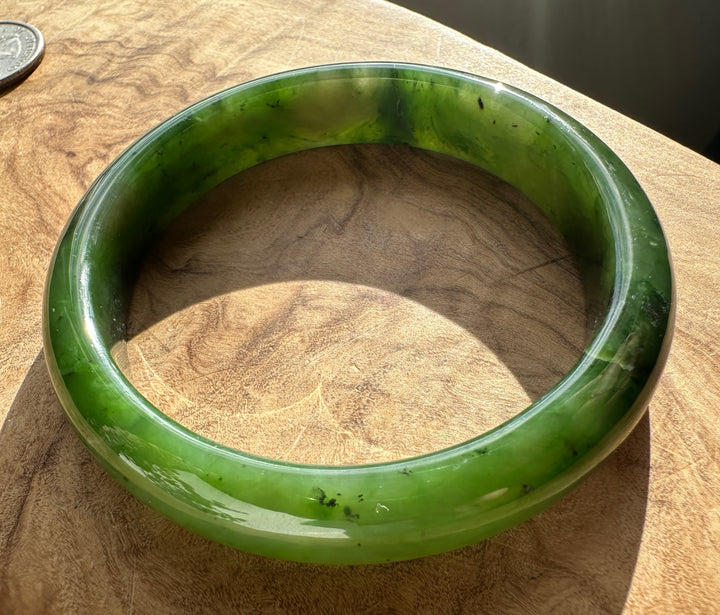 Interior of the green jade bangle showing a polished surface on wood with a coin nearby.