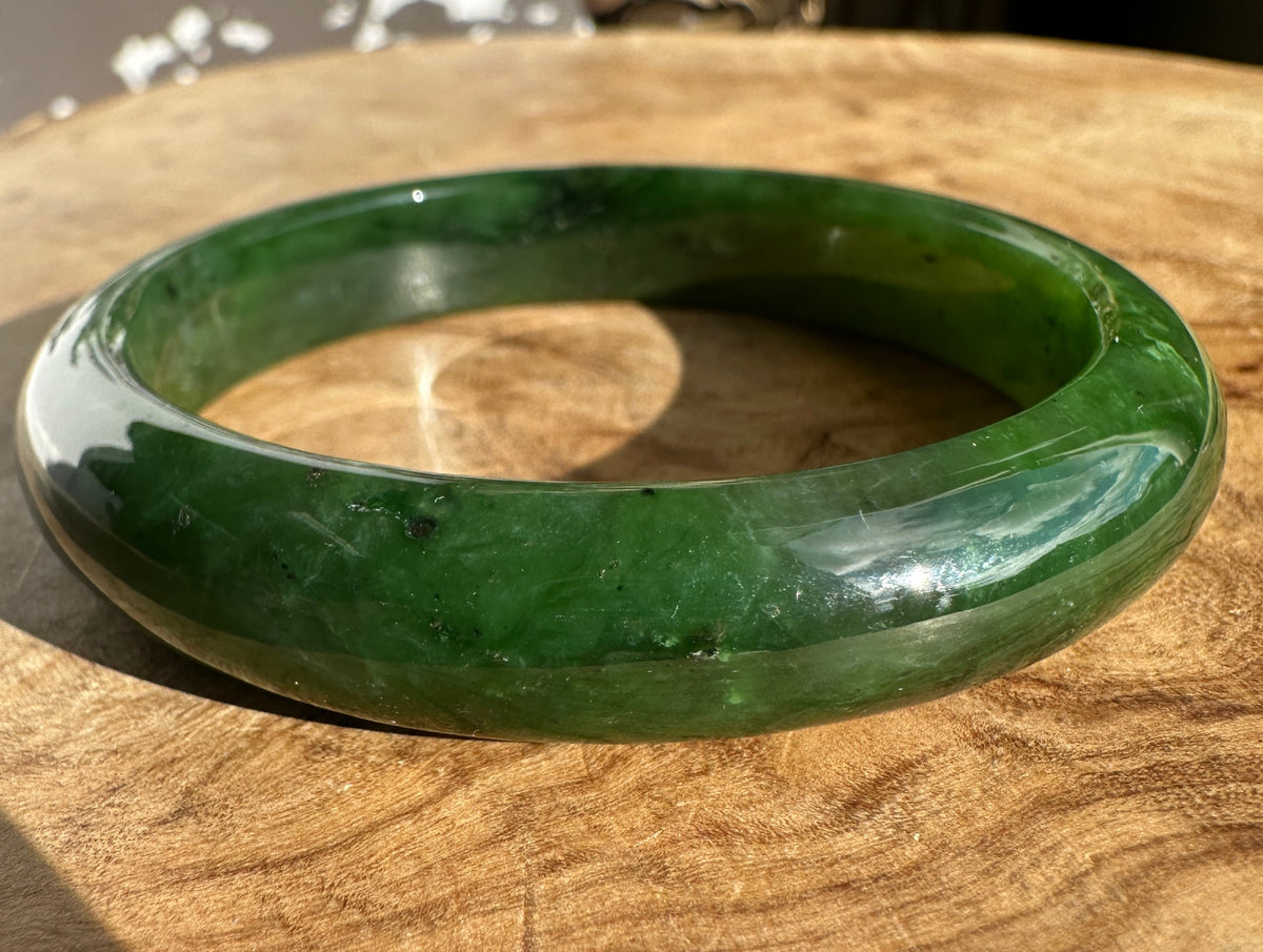 Close up of a green jade bangle showing its inner curve and natural color variations on wood
