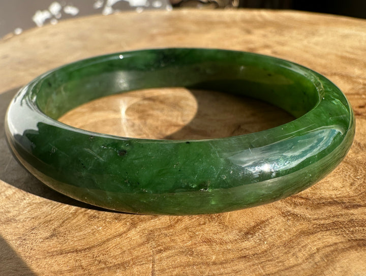 Close up of a green jade bangle showing its inner curve and natural color variations on wood