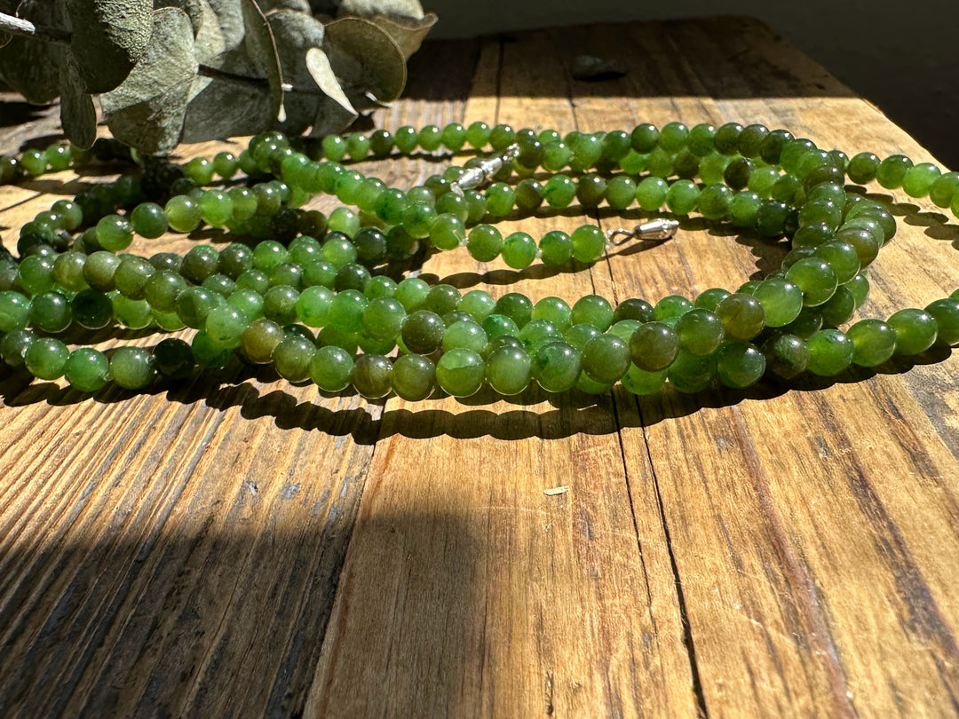 Close-up of several strands of 5mm Canadian nephrite jade beads on a wooden surface