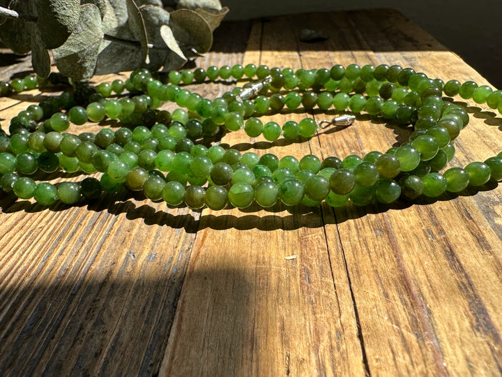 Close-up of several strands of 5mm Canadian nephrite jade beads on a wooden surface