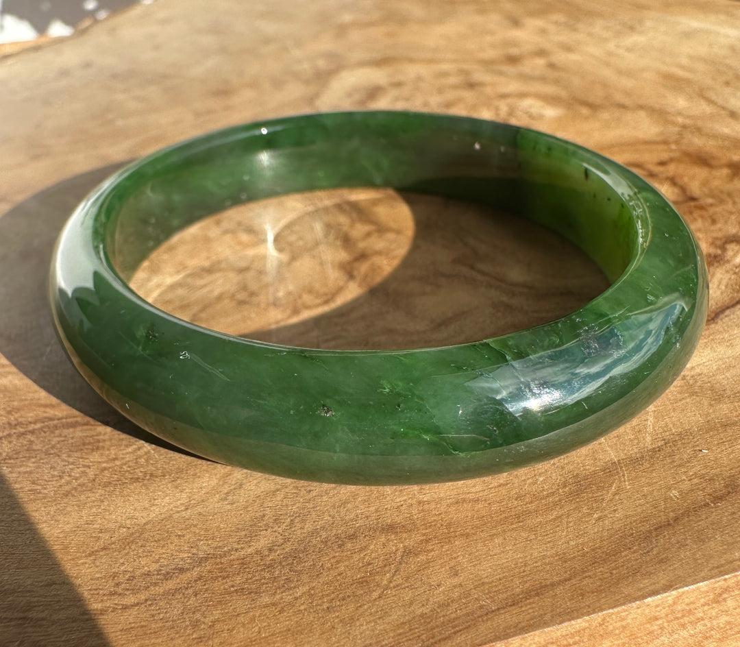 Jade Bangle 55.5 x 12mm in deep green resting on a wooden surface