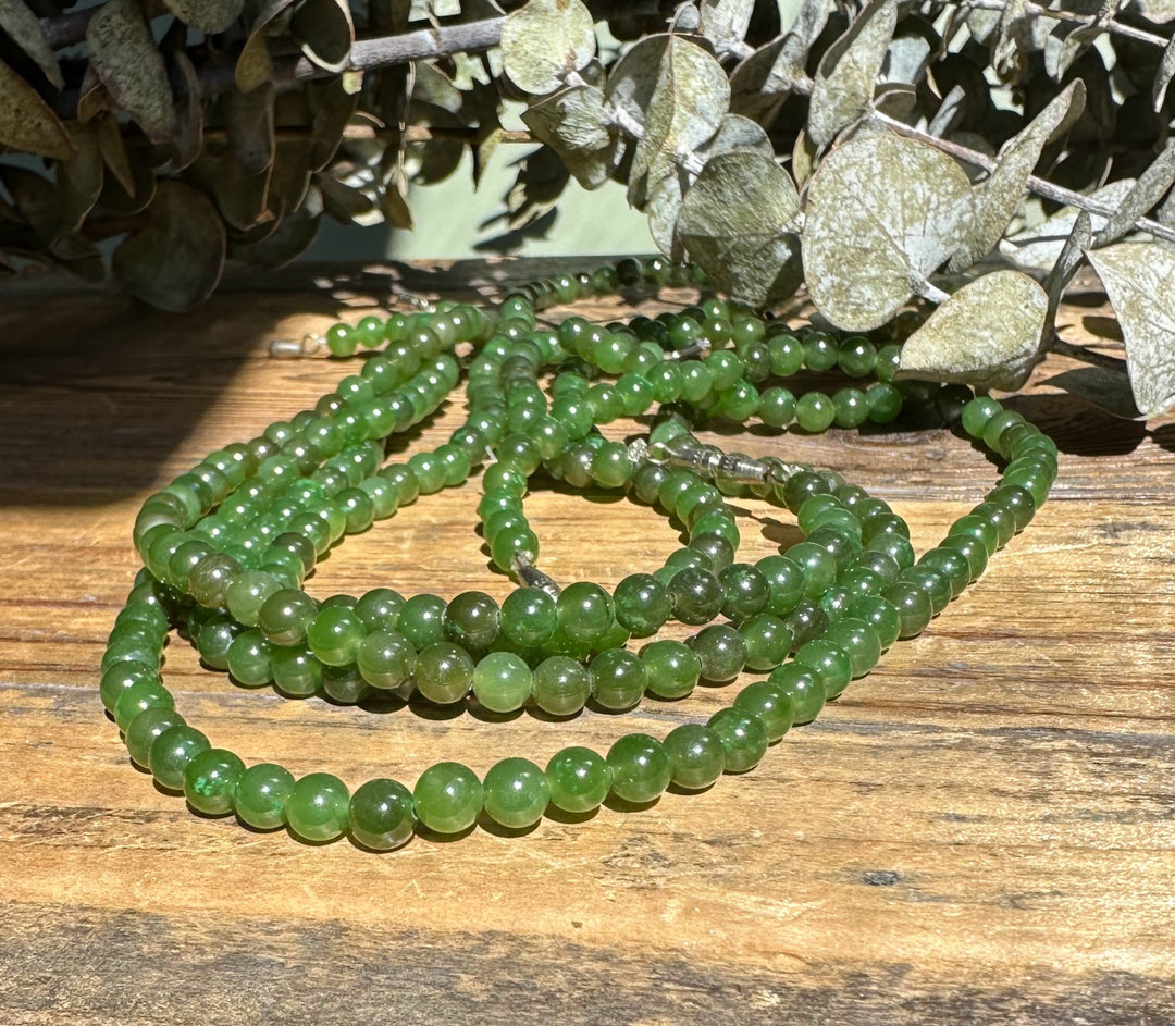 5mm Canadian nephrite jade beads arranged on a rustic wooden surface with dried leaves in the background