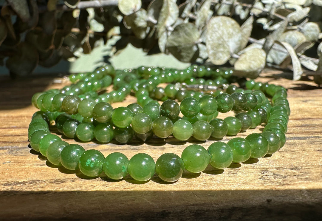 Cluster of 5mm Canadian nephrite jade beads in varying green shades arranged on a wooden surface
