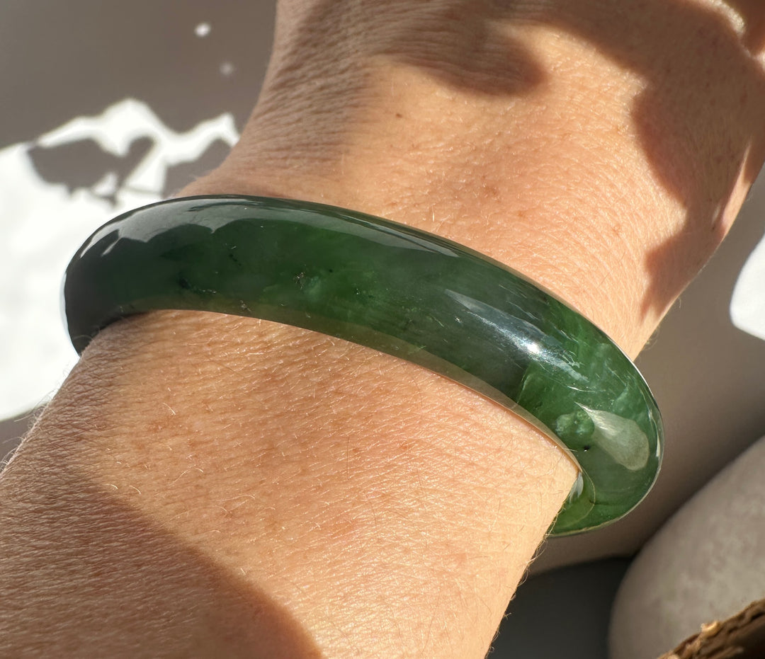 Deep green jade bangle worn on the wrist with a glossy polished surface