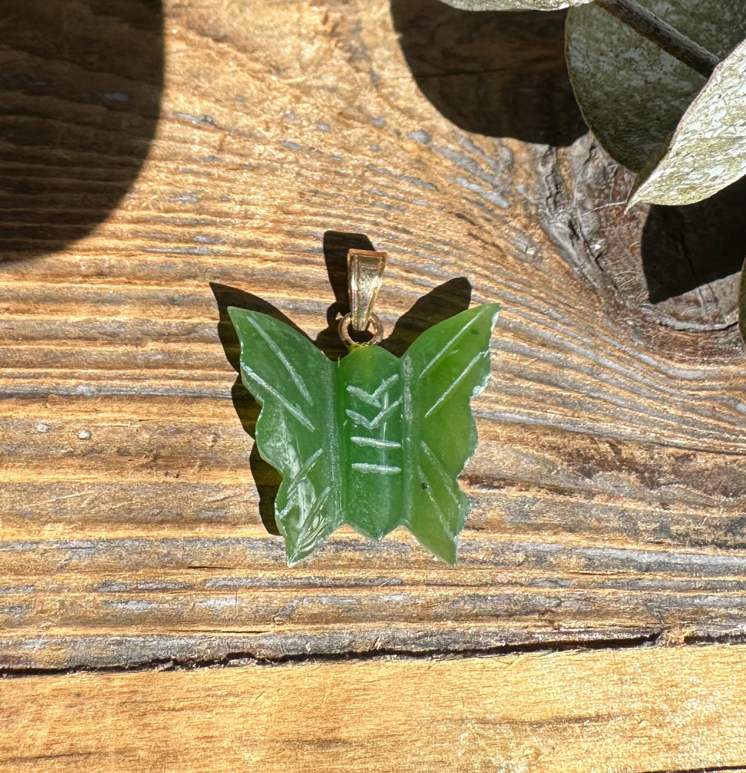 Vintage jade butterfly pendant 20mm with carved wings and gold bail on wood surface.
