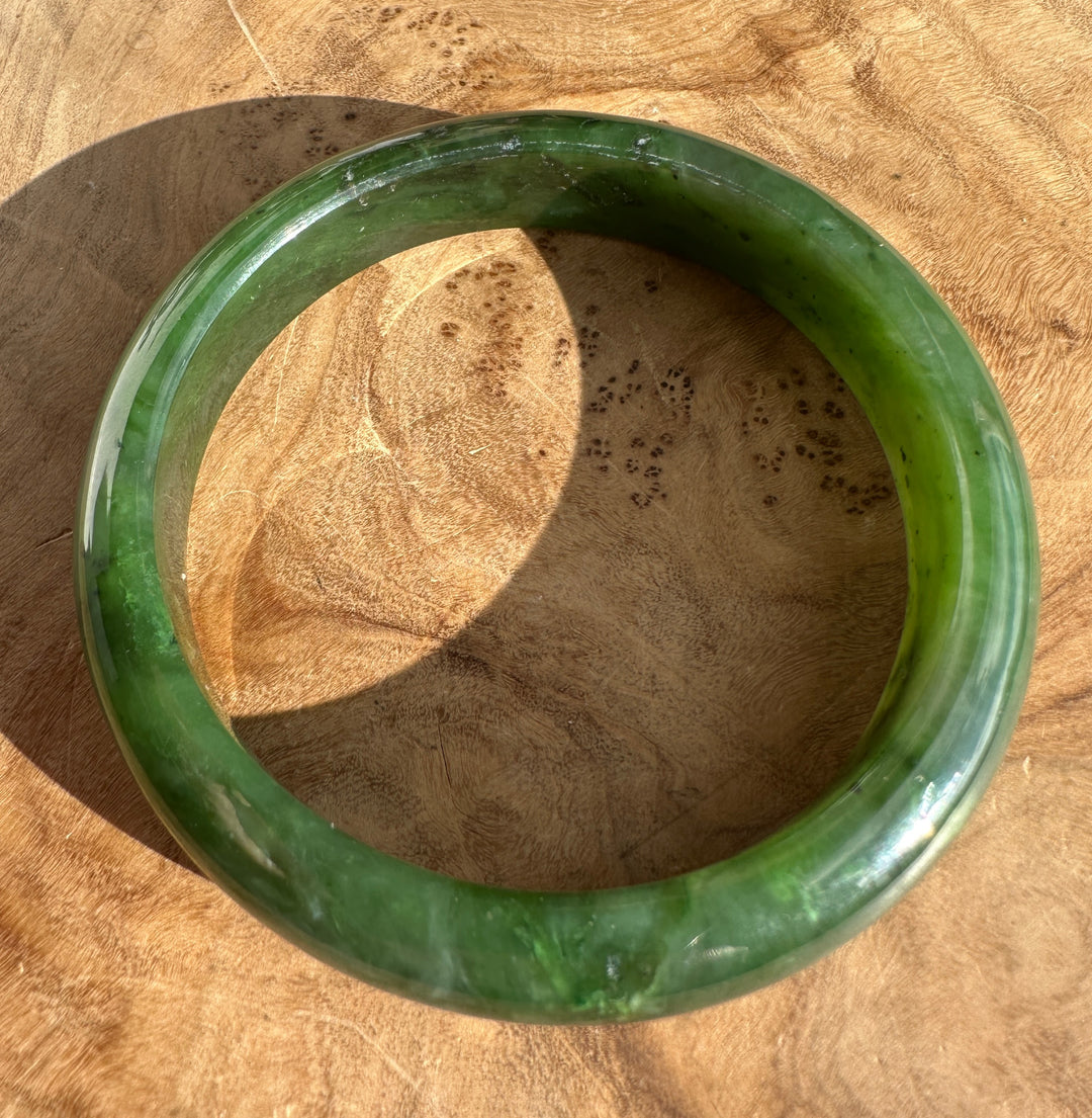 Glossy green jade bangle resting on a wooden surface.