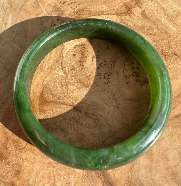 Glossy green jade bangle resting on a wooden surface.