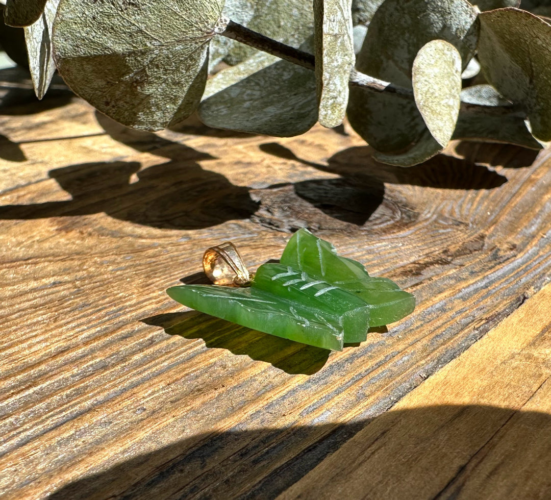 Close-up of jade butterfly pendant 20mm with gold bail on weathered wood.