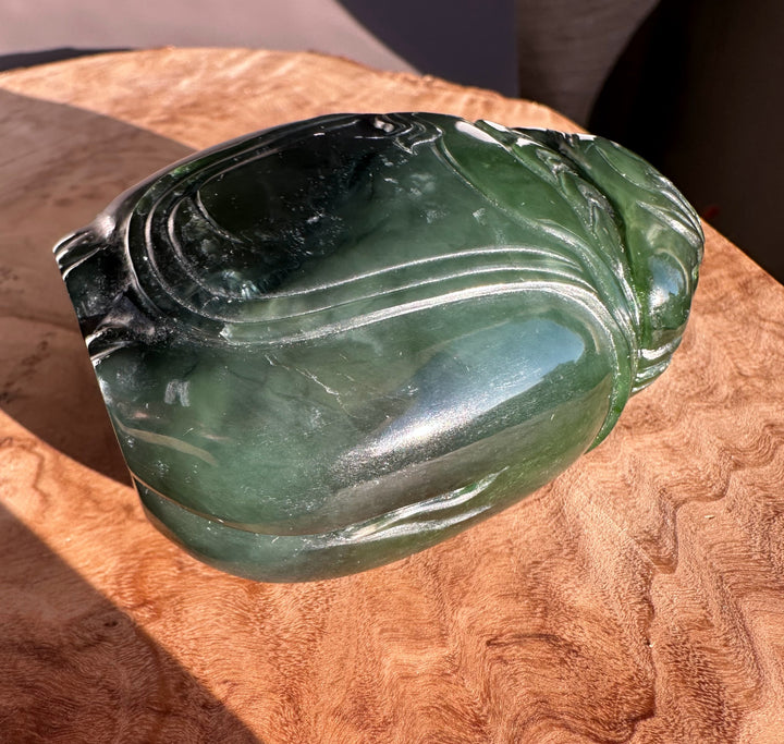 Jade carving of a young boy riding an elephant in dark green stone with flowing carved lines