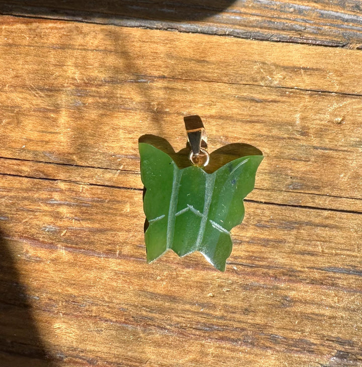 Back view of green jade butterfly pendant 20mm with gold bail on wooden surface.