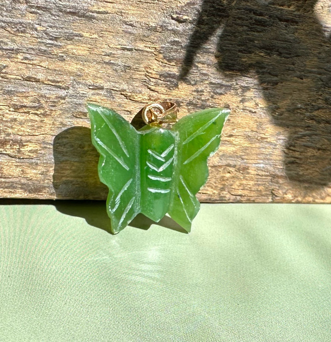 Green jade butterfly pendant with a gold bail on a wooden surface