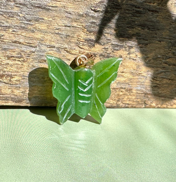 Green jade butterfly pendant with a gold bail on a wooden surface