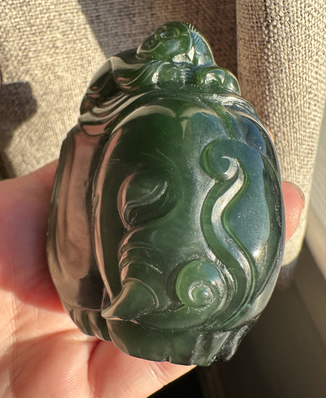 Side view of a green jade carving with swirling patterns and a rider perched on top