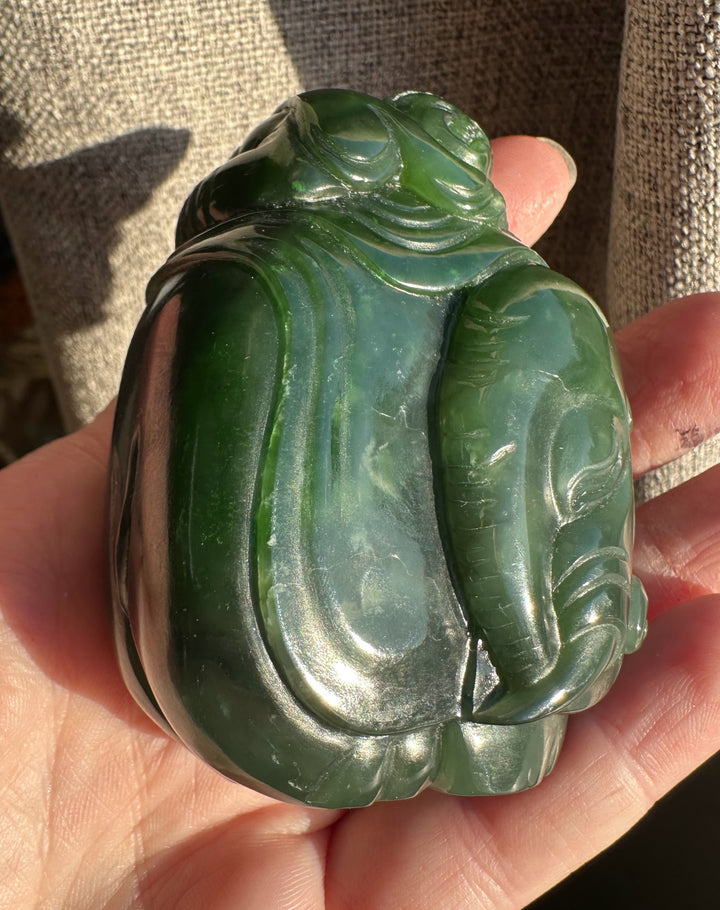 Green jade carving of a young boy riding an elephant shown in side view.