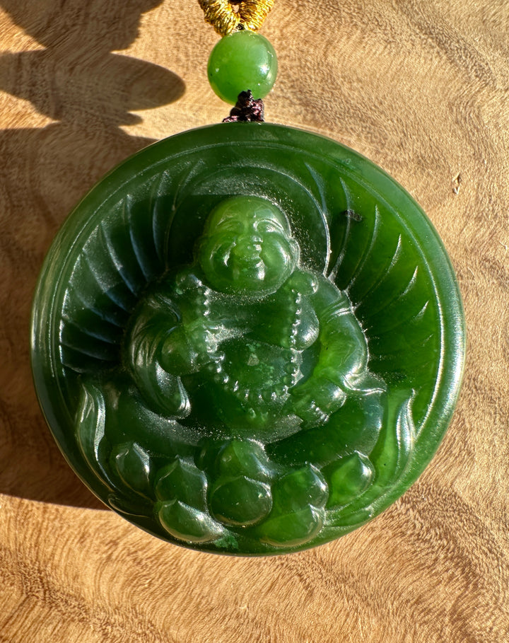 Close up of jade Buddha lotus pendant on black cord with a gold wrap and a green bead above the round carved disc.