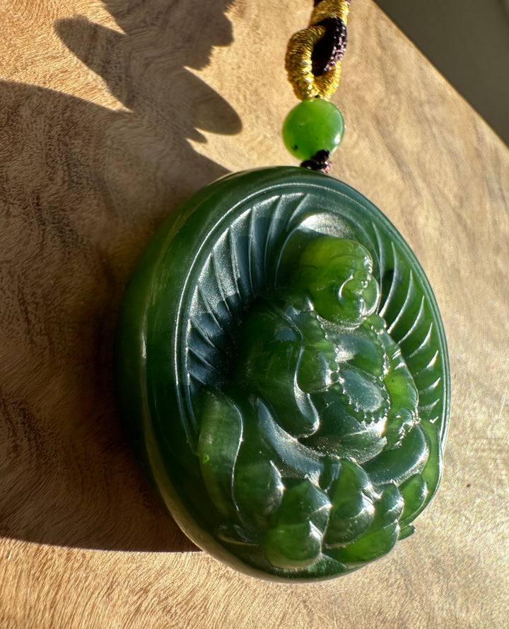 Green nephrite jade Buddha lotus pendant with carved Buddha figure on a round disc and yellow knotted cord.