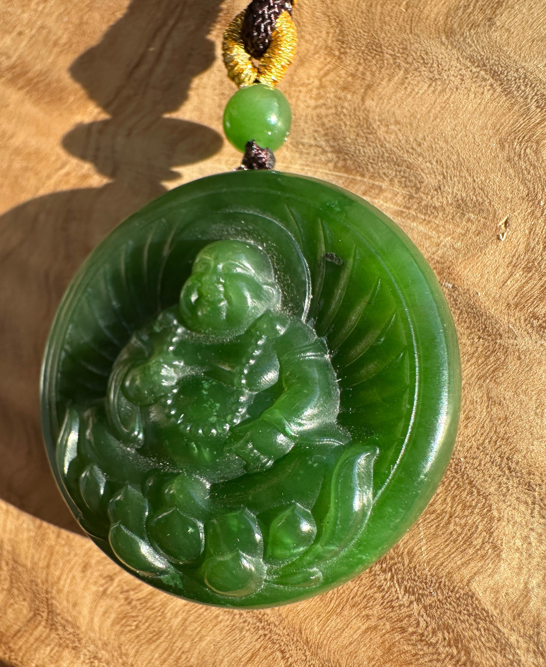 Front view of round green jade Buddha Lotus pendant with carved details and cord on a wooden surface