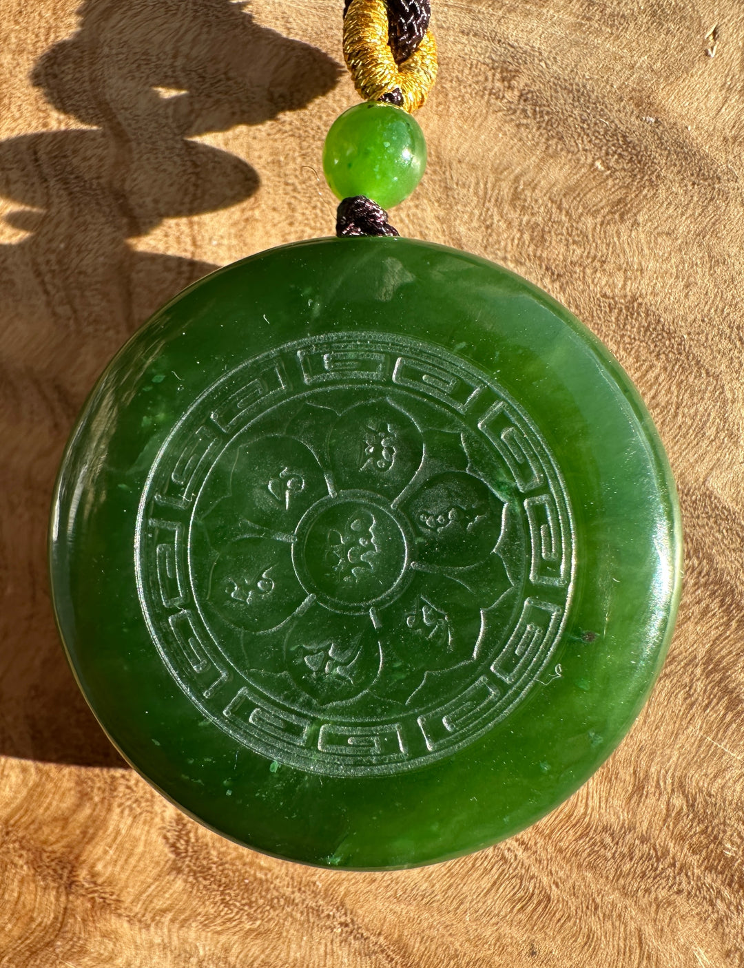 Green nephrite jade Buddha Lotus pendant on a golden braided cord against a sand colored background