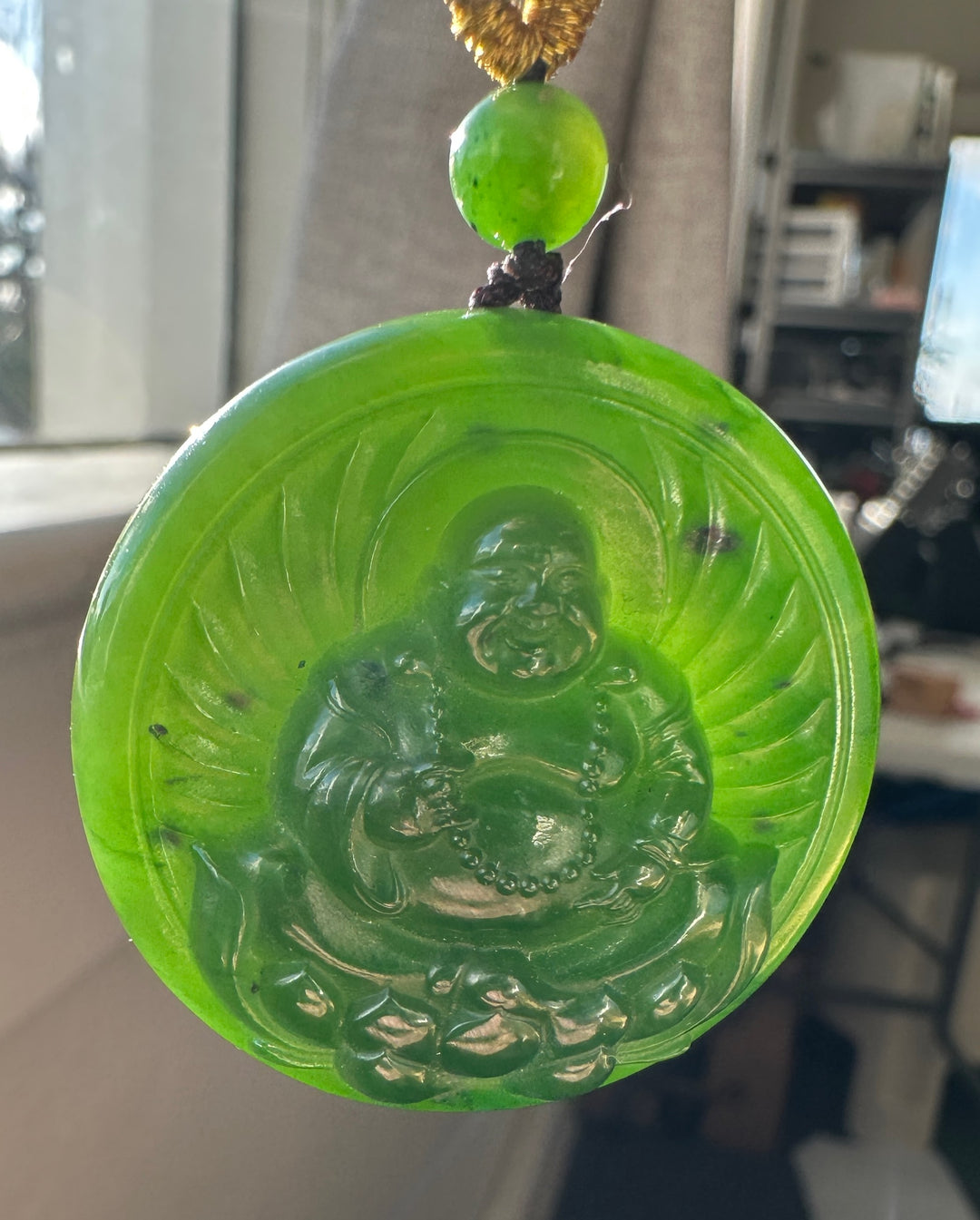 Close up of the Buddha Lotus pendant showing a green bead and golden braided cord with knot against a workshop background
