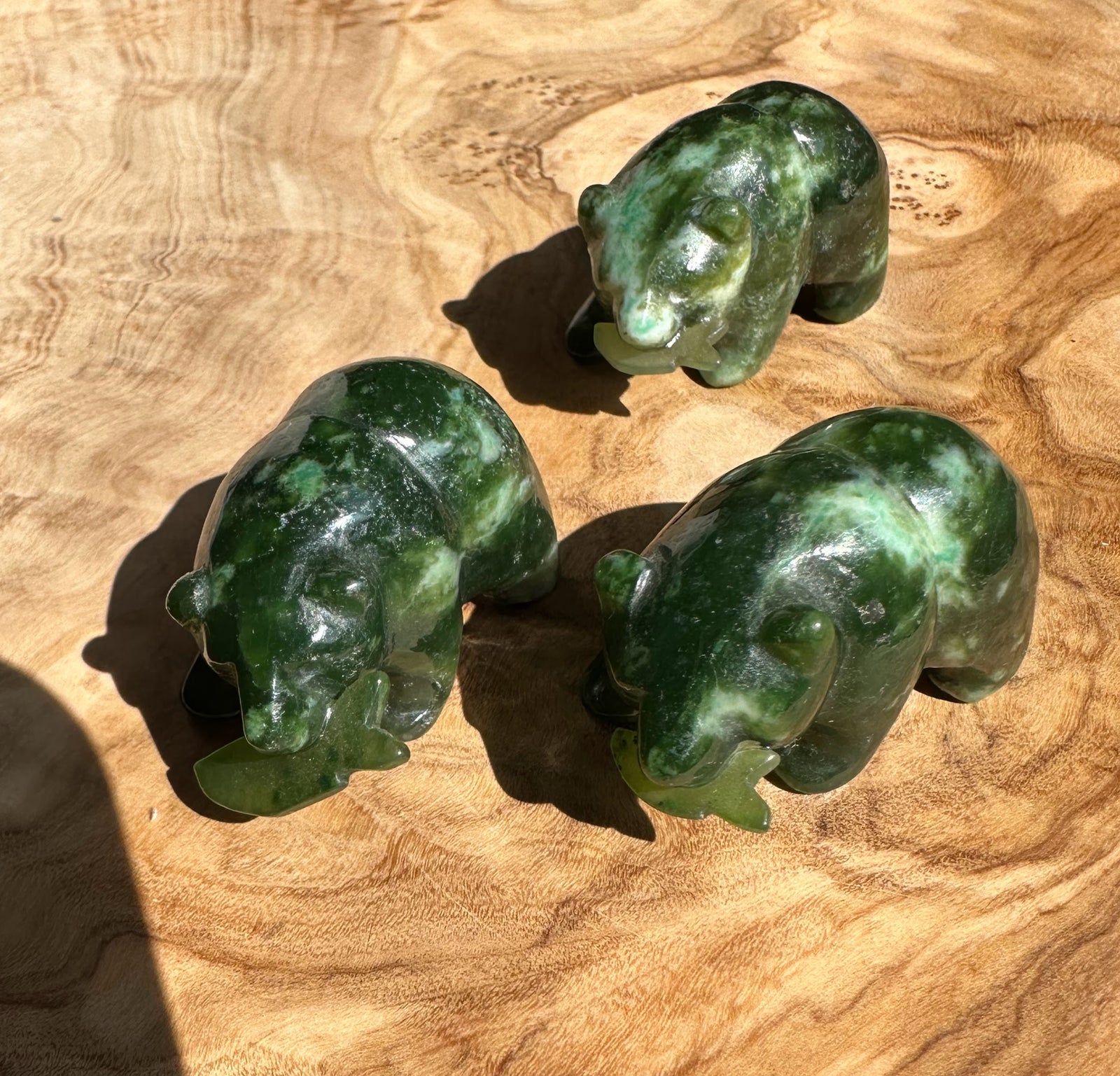 Three jade bear carvings with a jade fish between them on a wooden surface.