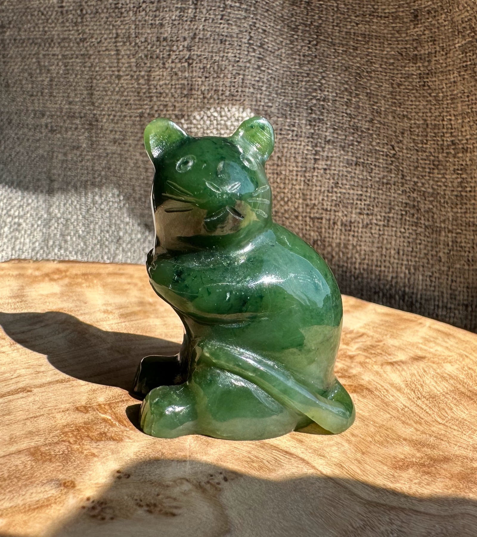 Green jade mouse figurine sitting on a wooden surface with a brown textured backdrop.