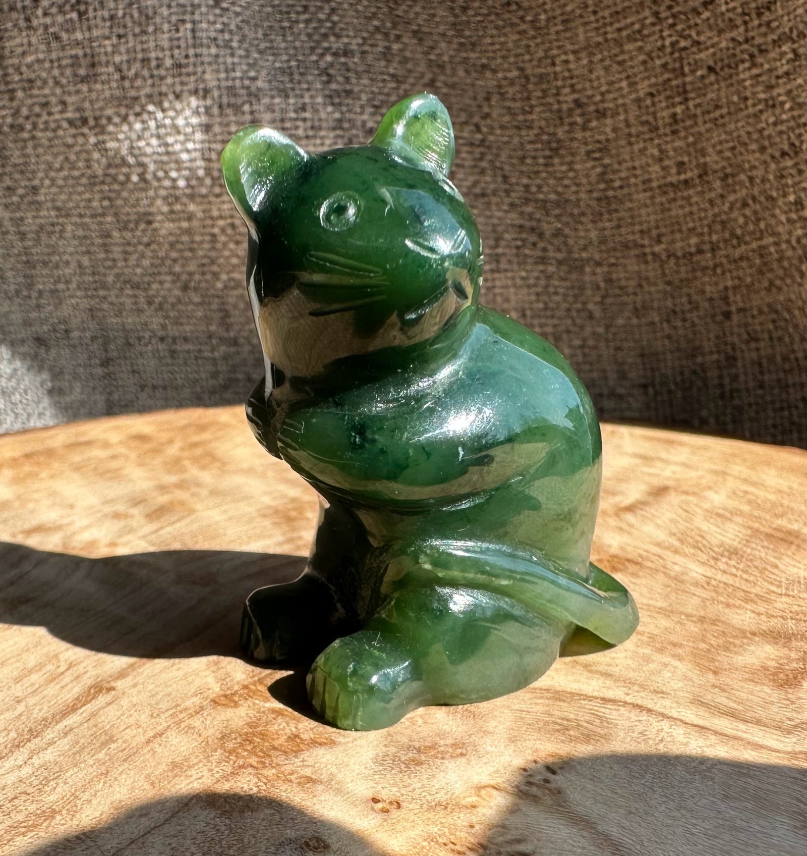 Side view of a green jade mouse figurine on a sunlit wooden surface.