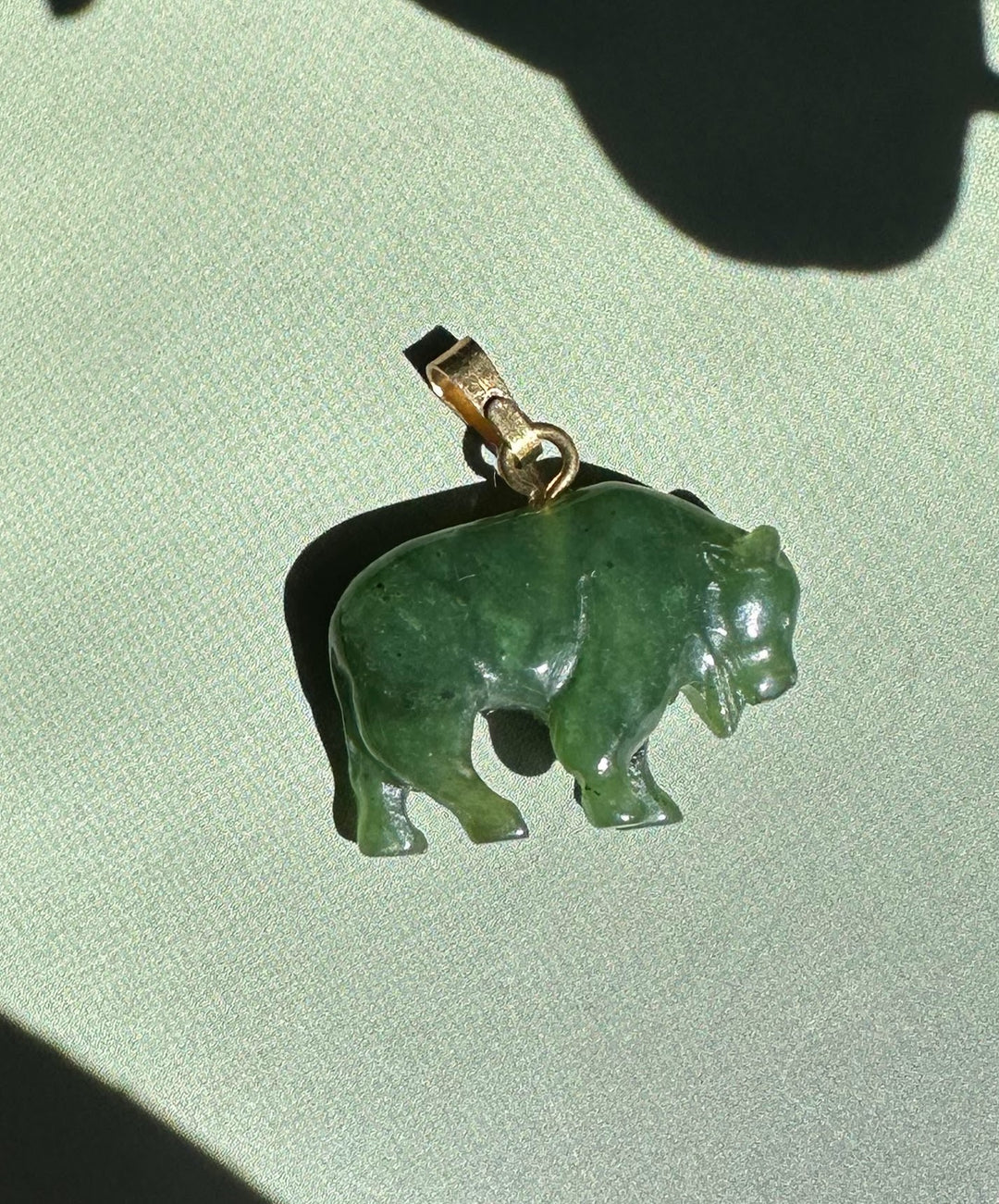 Canadian Jade Bison Charm pendant in green jade with a metal bail on a light background