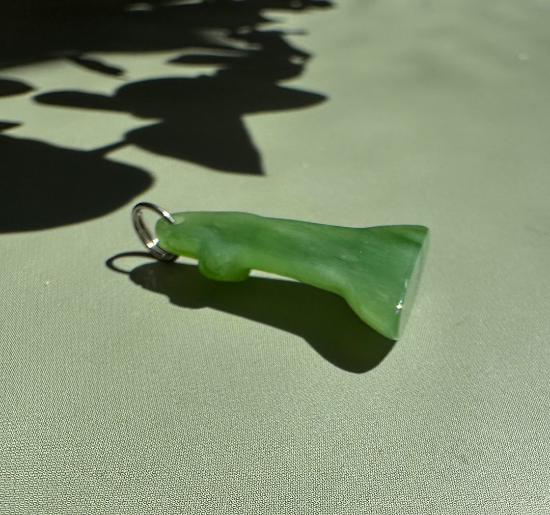 Green jade lighthouse charm with silver ring resting on pale green surface