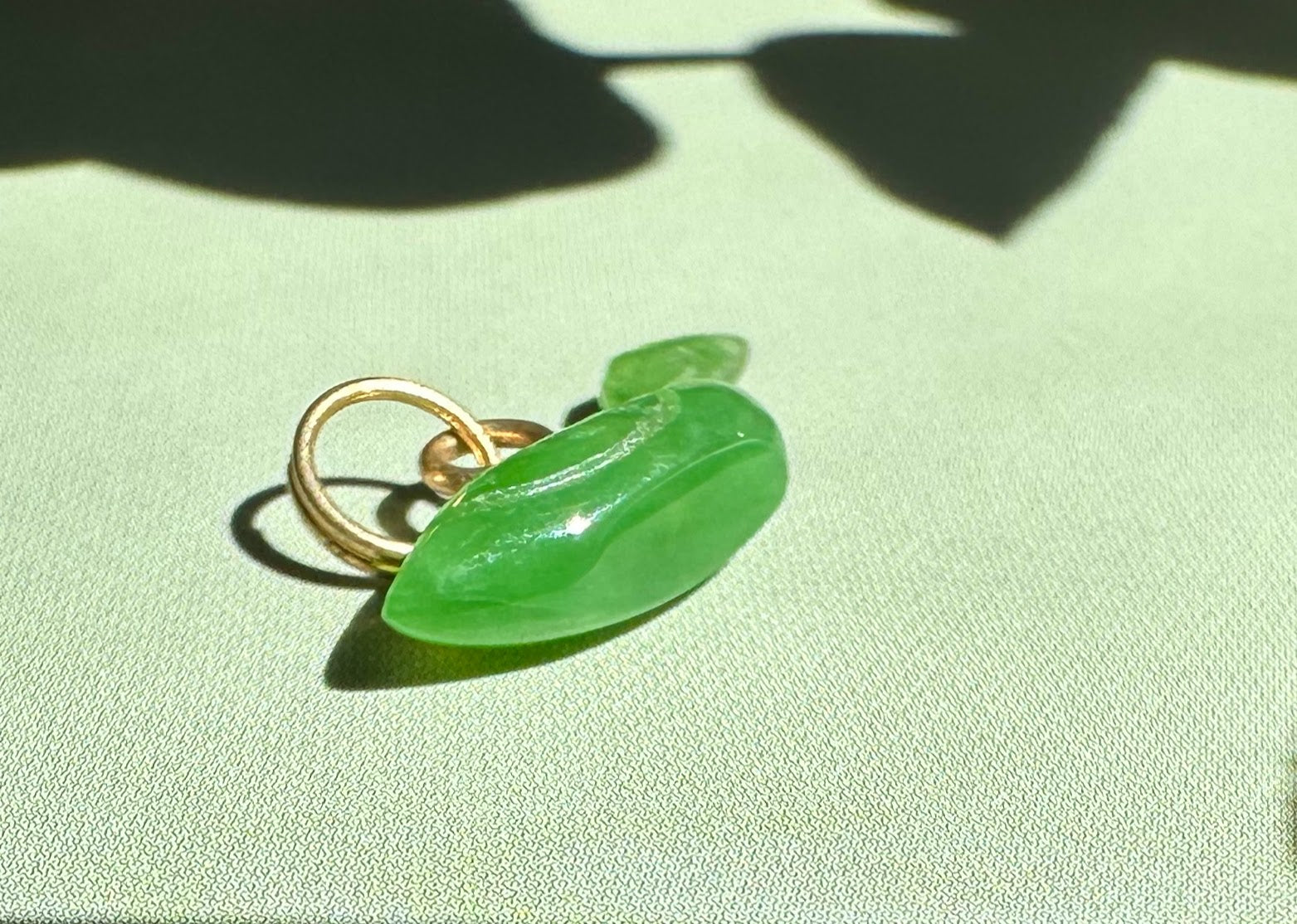 Siberian Jade Duck Charm 17mm viewed from side with gold ring bail on green surface