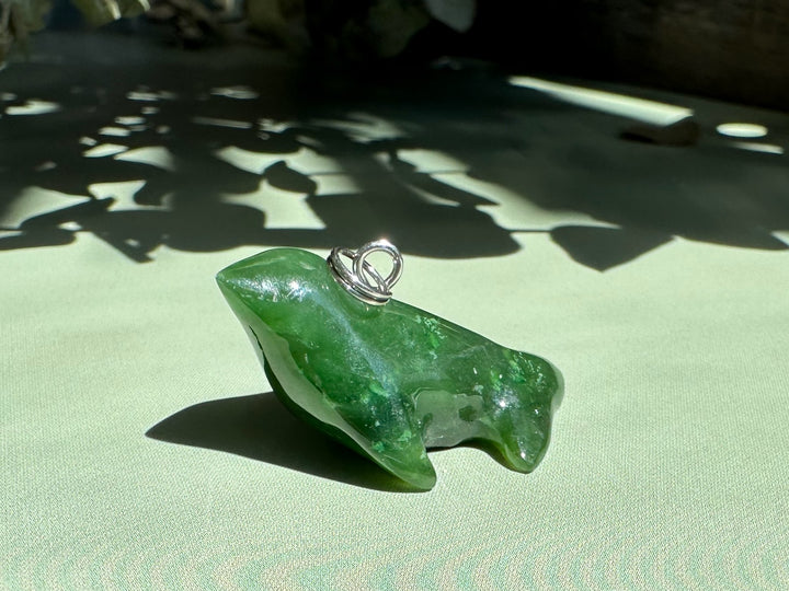 Green jade seal charm on a silver bail resting on a pale green surface