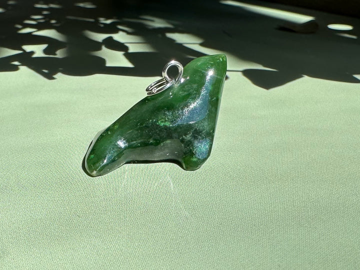 One inch green jade seal charm with a silver loop for necklace on a pale green surface.
