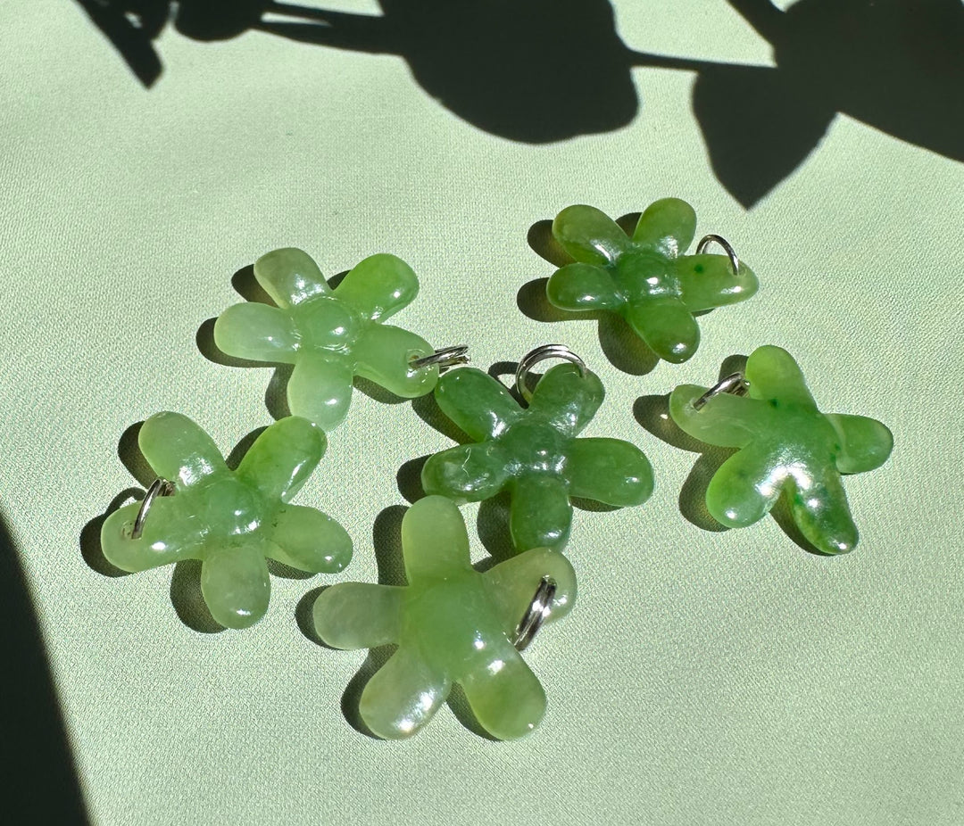 Several jade flower charms with silver loops laid out on a pale surface