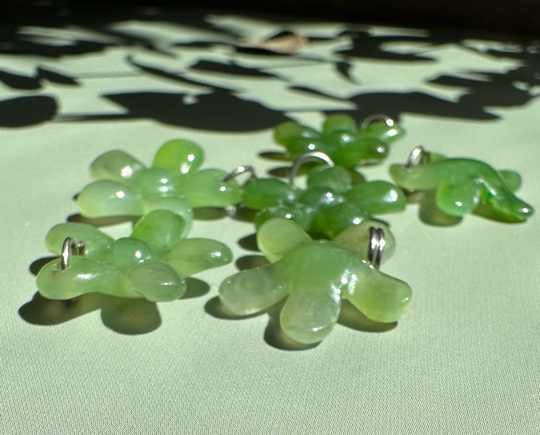 Light green jade flower charms with silver loops scattered on a pale surface
