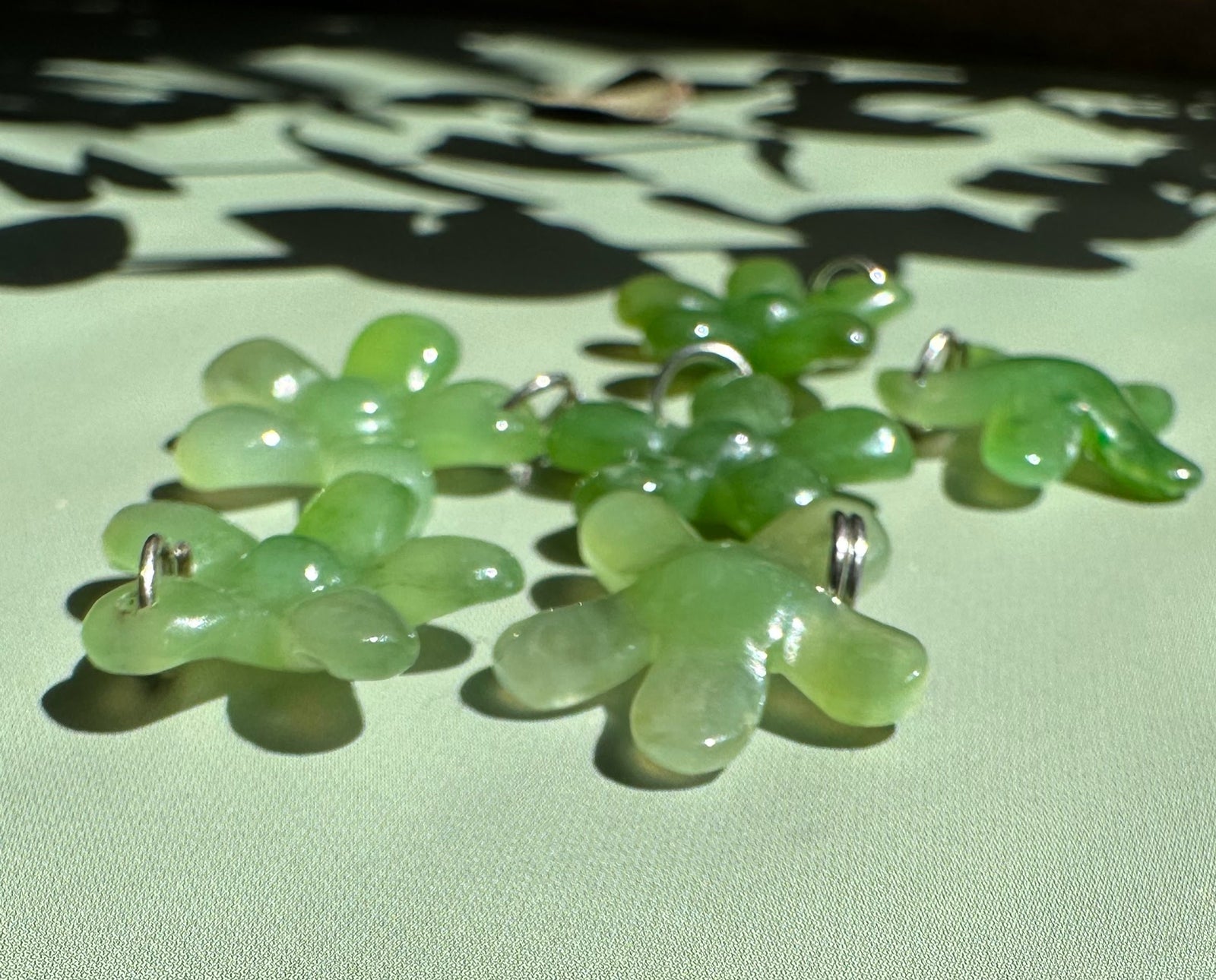 Light green jade flower charms with silver loops scattered on a pale surface