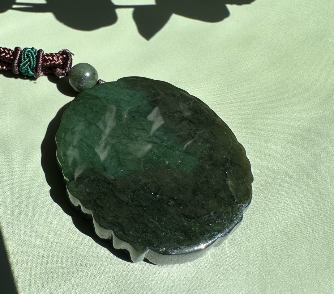 Canadian Jade Ku Lou pendant with a scalloped edge in deep green on a brown braided cord
