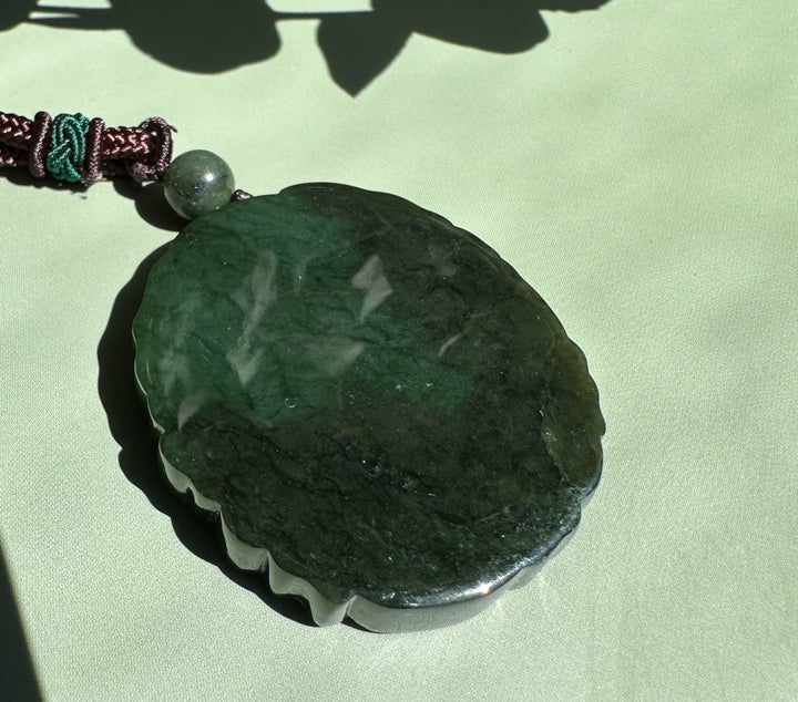 Canadian Jade Ku Lou pendant with a scalloped edge in deep green on a brown braided cord
