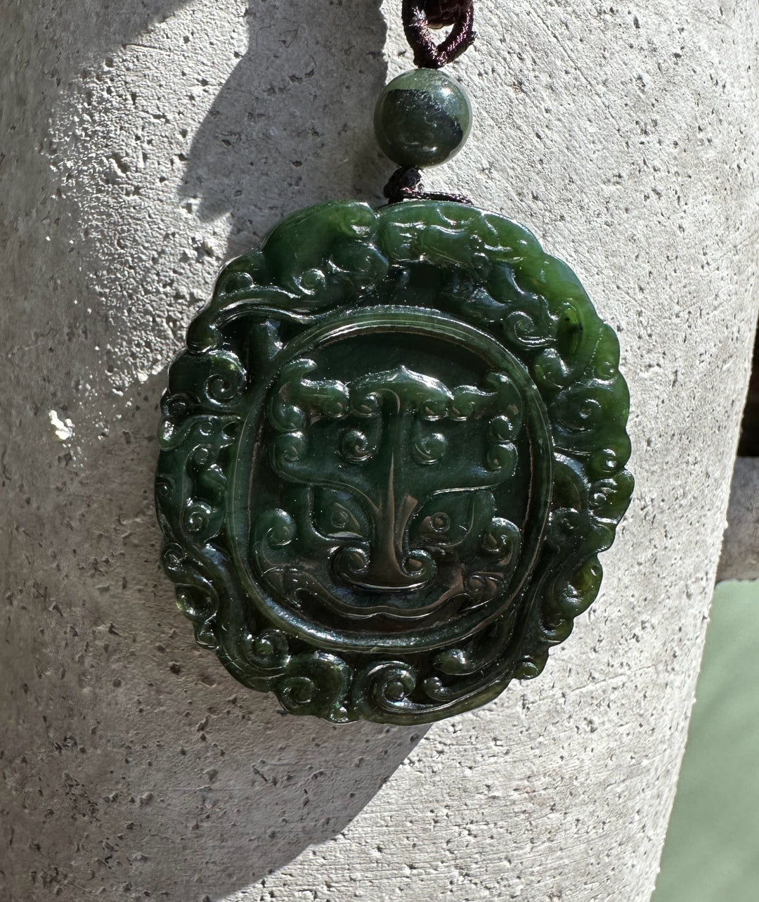 Canadian jade Ku Lou pendant with carved face on a round medallion and braided cord