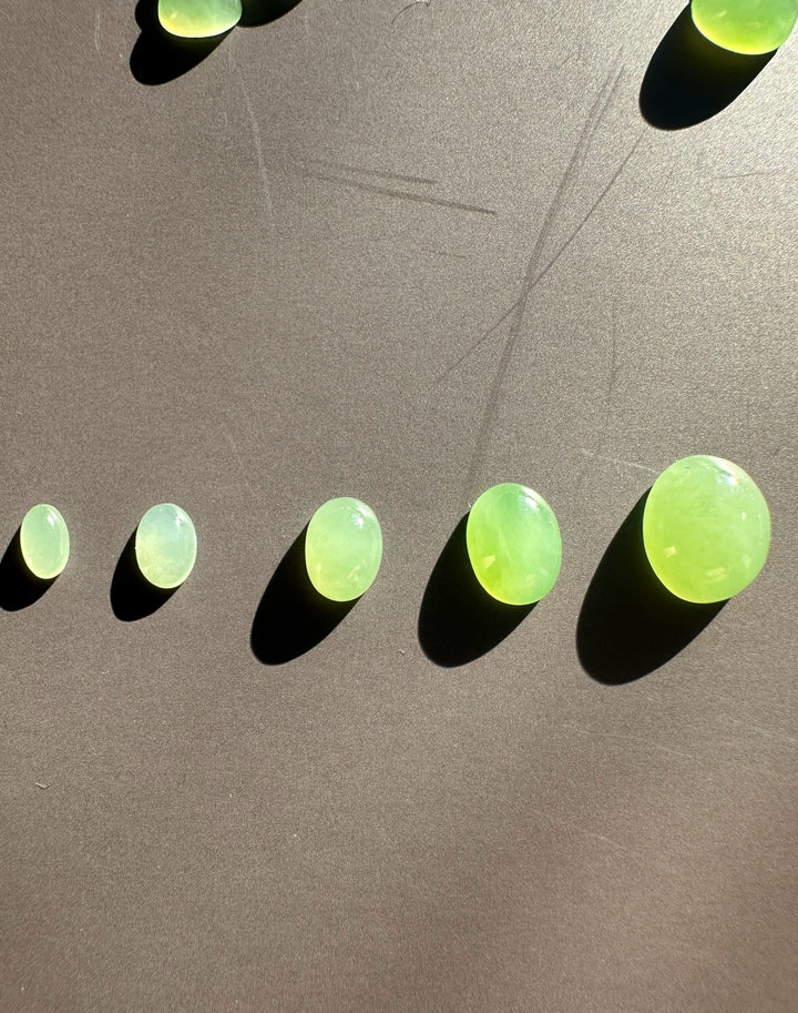 Line of apple green oval cabochons on a dark surface with strong shadows.