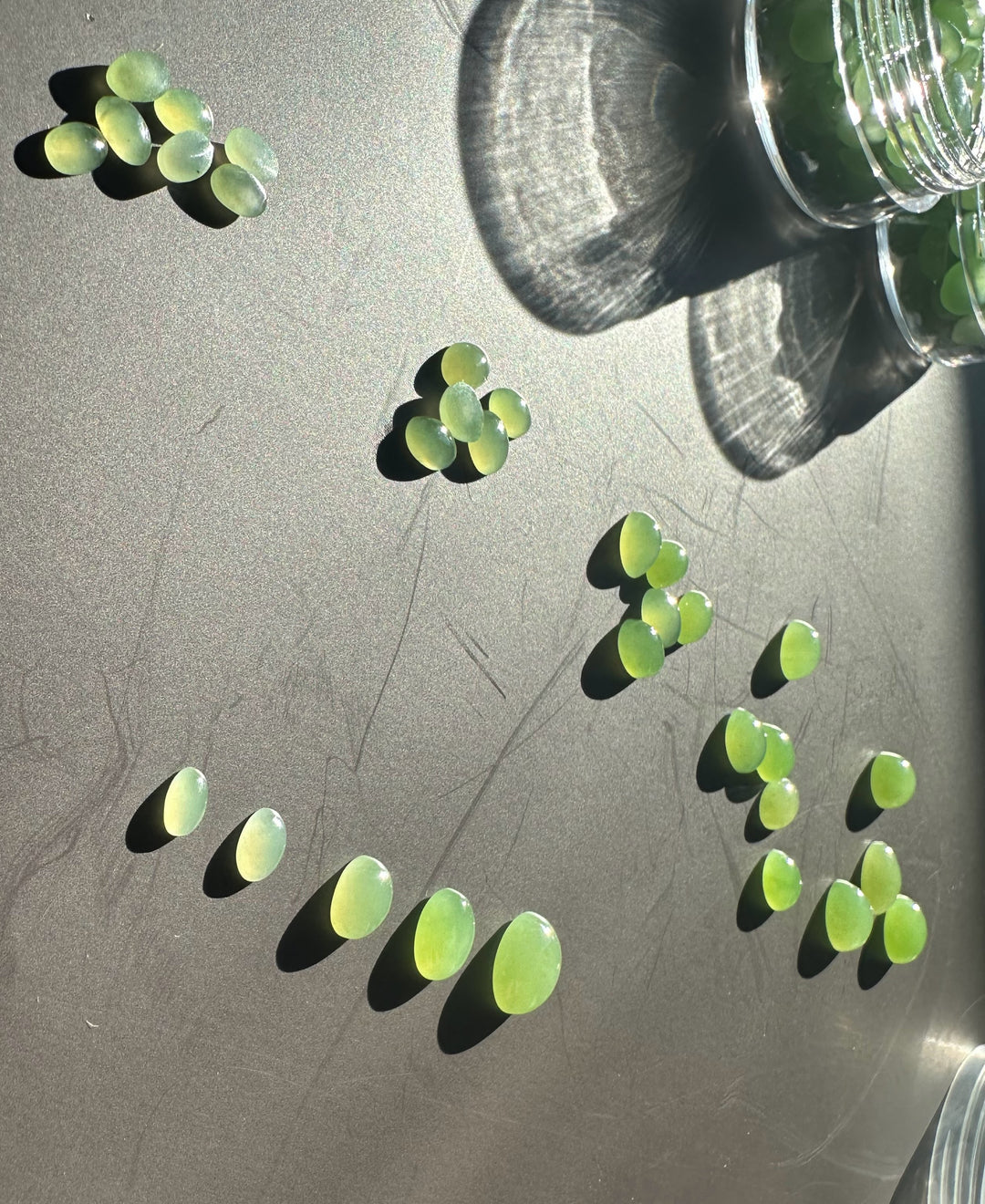 Assorted apple green oval cabochons in varying sizes scattered on a dark tabletop near a glass jar.