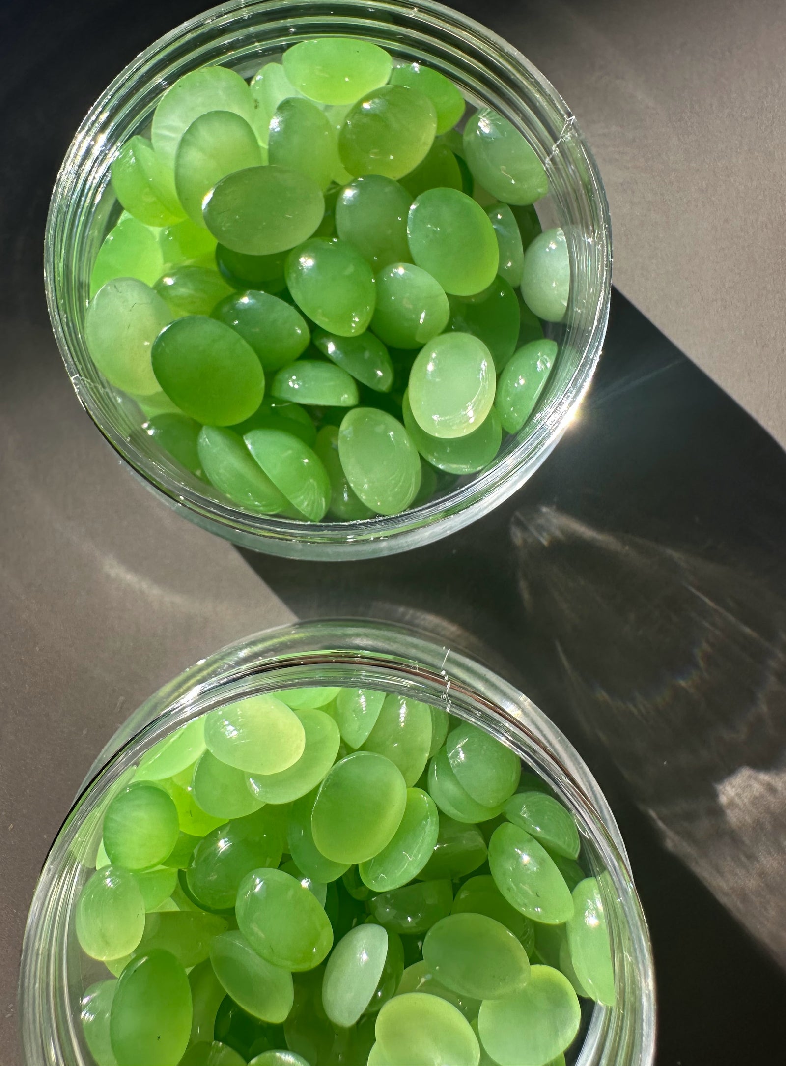 Two glass jars filled with numerous AA Siberian apple green oval cabochons viewed from above