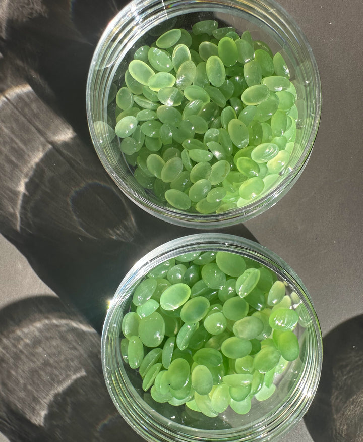 AA Siberian Apple Green oval cabochons in a clear glass jar