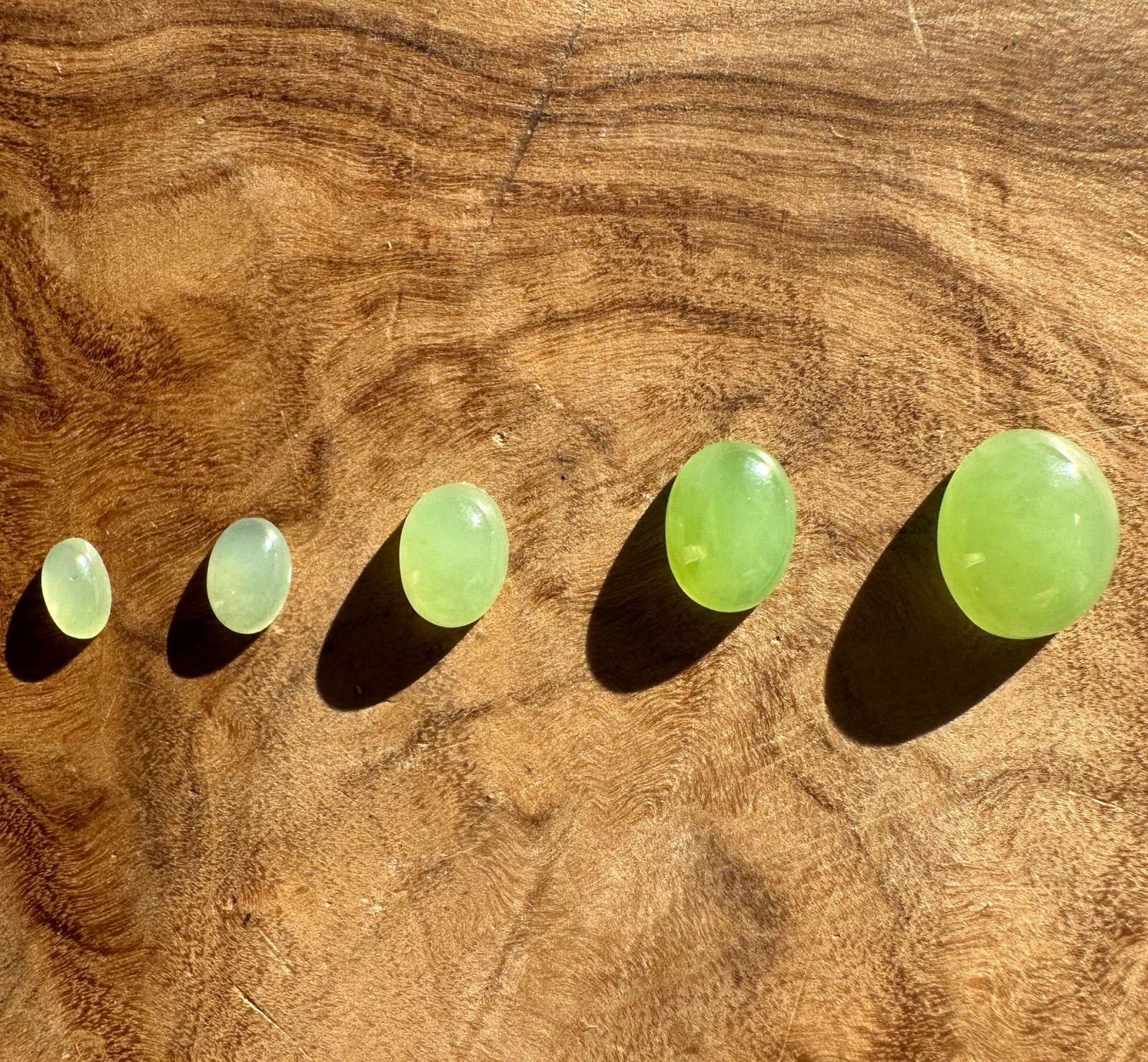 Five AA Siberian apple green oval cabochons arranged in a row on a wood surface