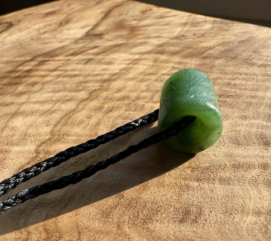 Green Canadian jade textured bead pendant on a black braided cord resting on a wood surface