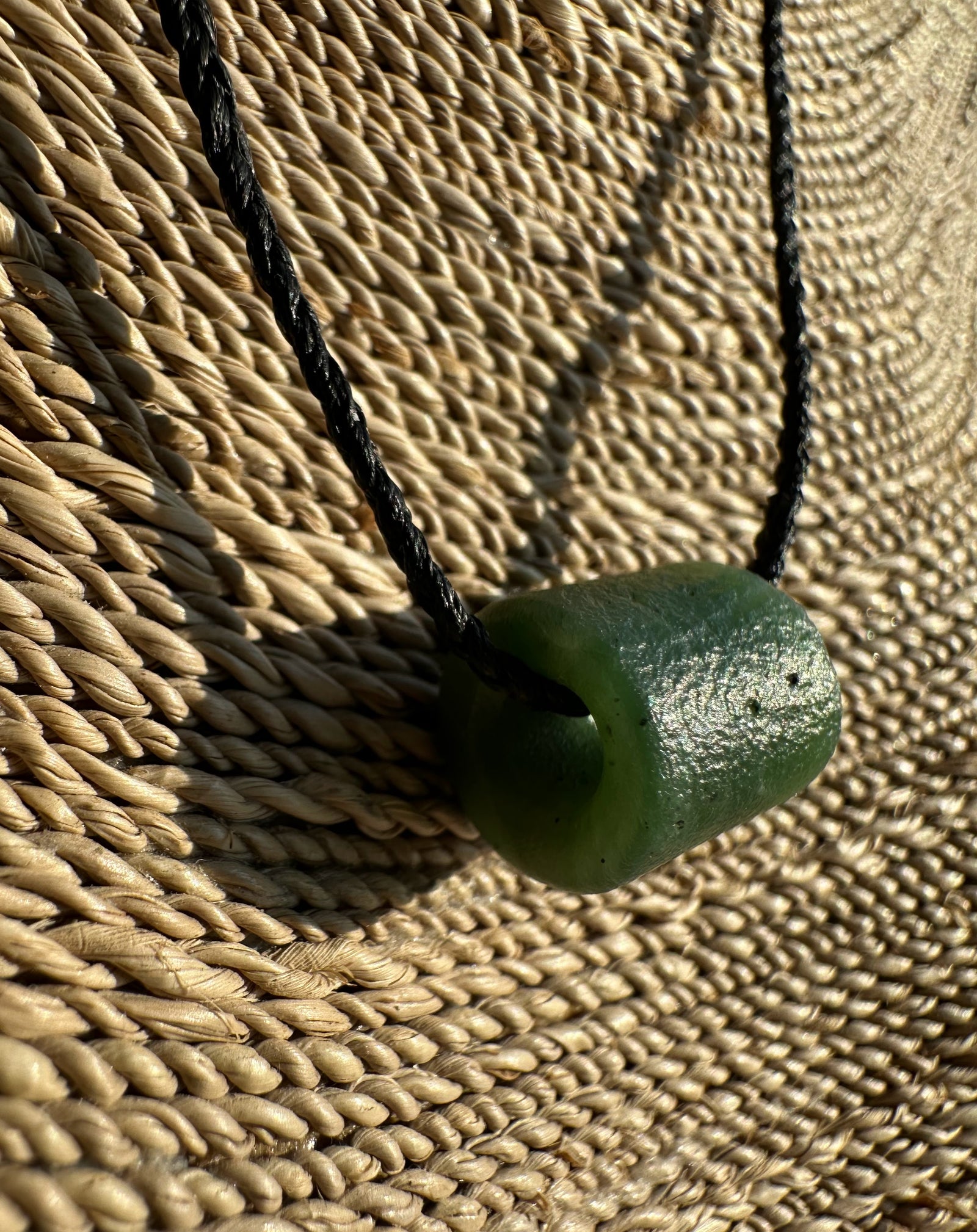 Canadian Jade textured bead pendant on a black braided cord against a woven straw background