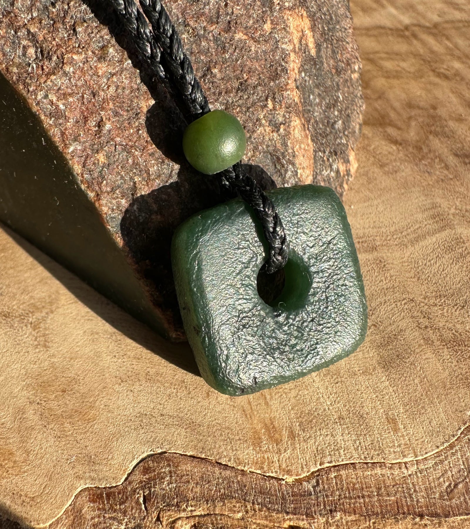 Canadian Jade textured square pendant 20mm threaded on a black cord showing the central hole and knot detail